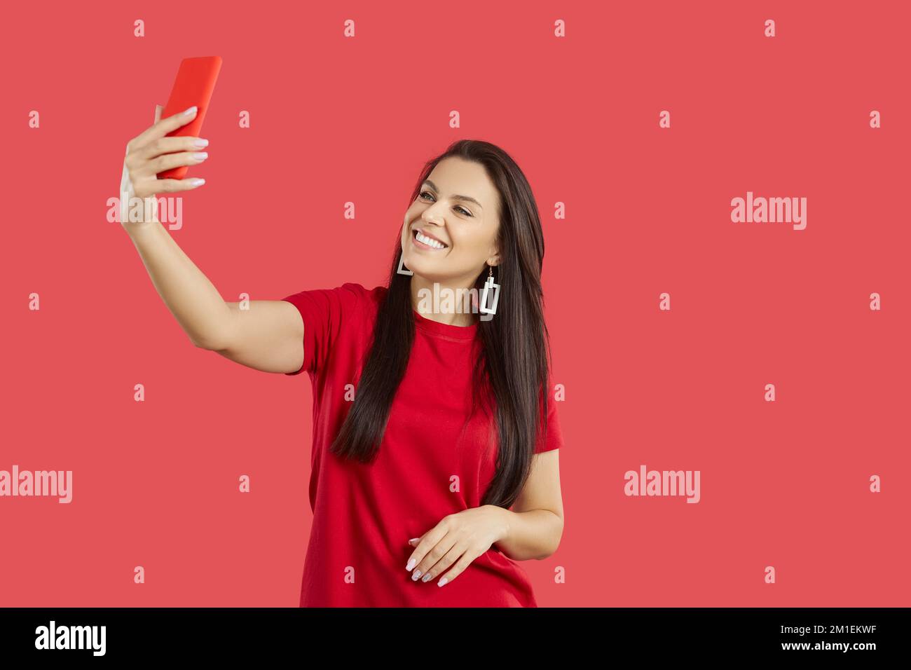 Bella giovane donna sorridente spensierata che fa selfie girato sul telefono cellulare su sfondo rosso. Foto Stock