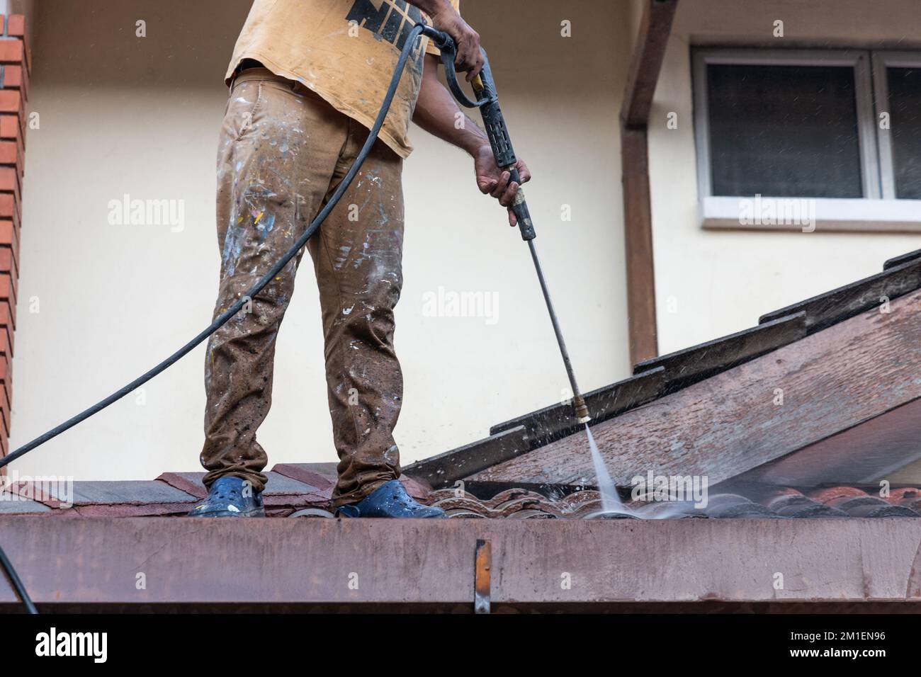 Lavoratore che utilizza una pistola a spruzzo ad acqua ad alta pressione per lavare e pulire lo sporco dalle piastrelle del tetto durante i lavori di ristrutturazione Foto Stock