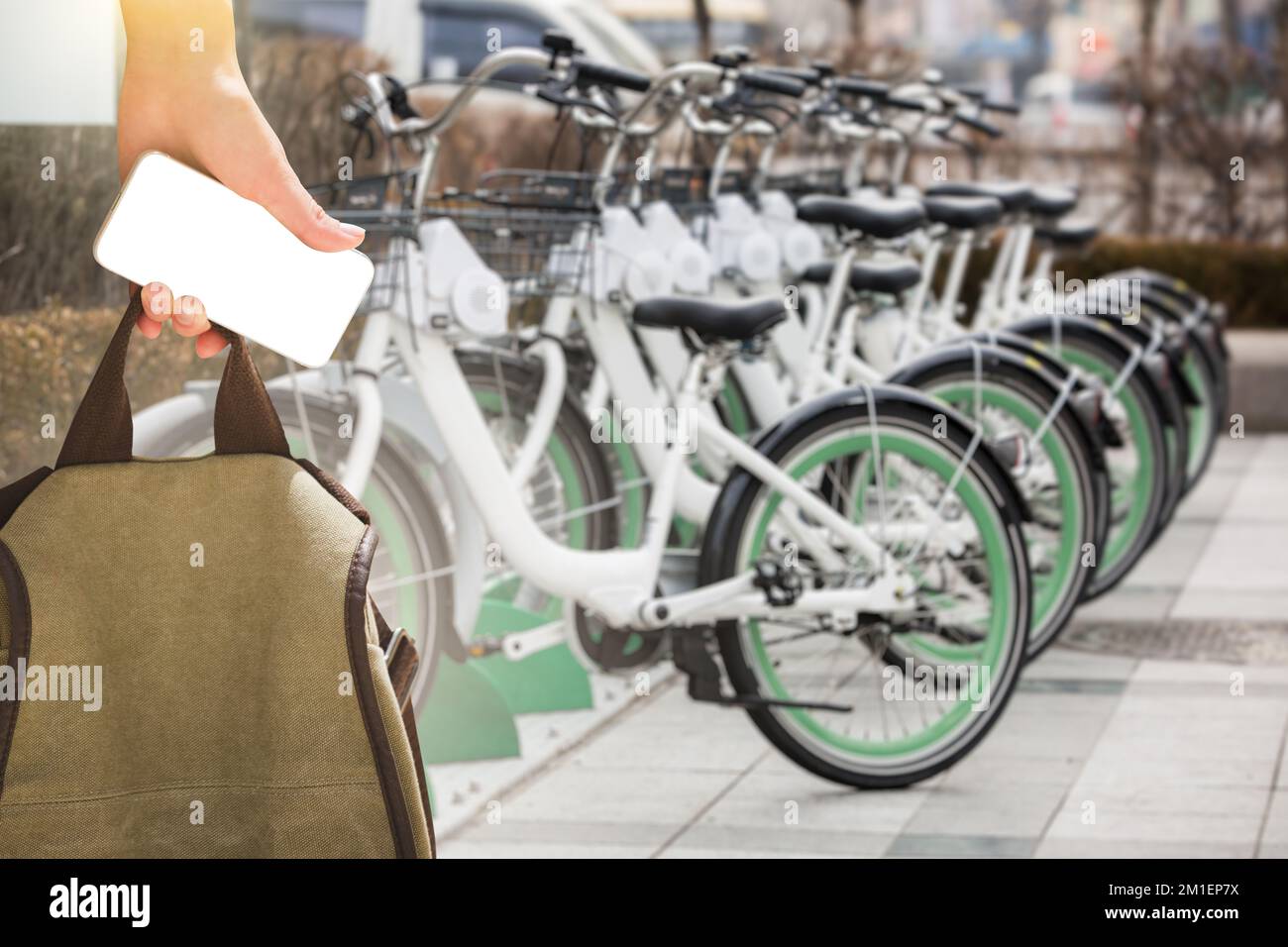 Primo piano di una mano con uno smartphone e uno zaino davanti a una fila di biciclette a noleggio. Schermo vuoto, è possibile incollare il contenuto Foto Stock