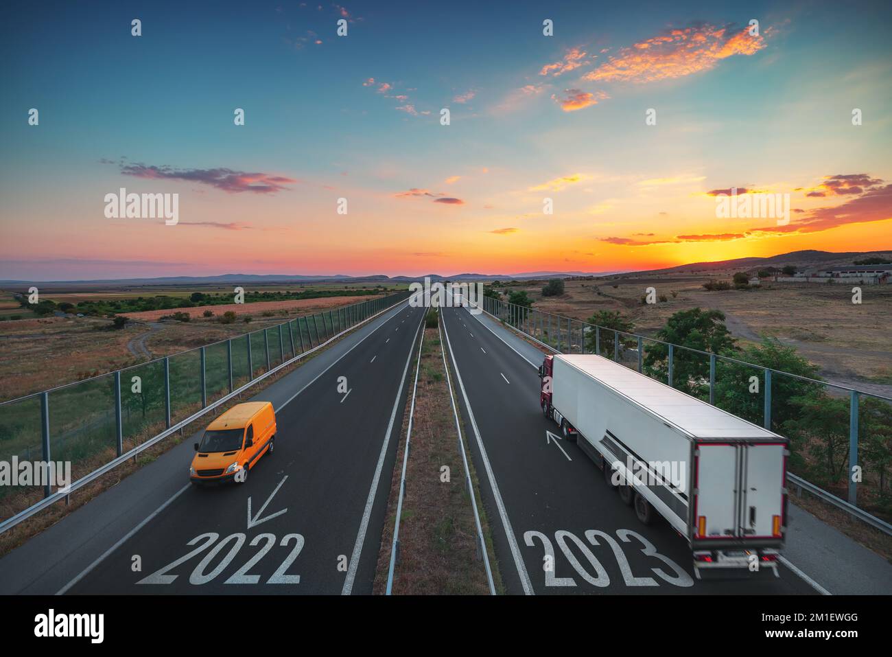 Guida su strada aperta verso il nuovo anno 2023 al tramonto. Vista aerea dell'autostrada, dell'auto, del furgone e del camion. Trasporto, logistica, concetto di viaggio Foto Stock