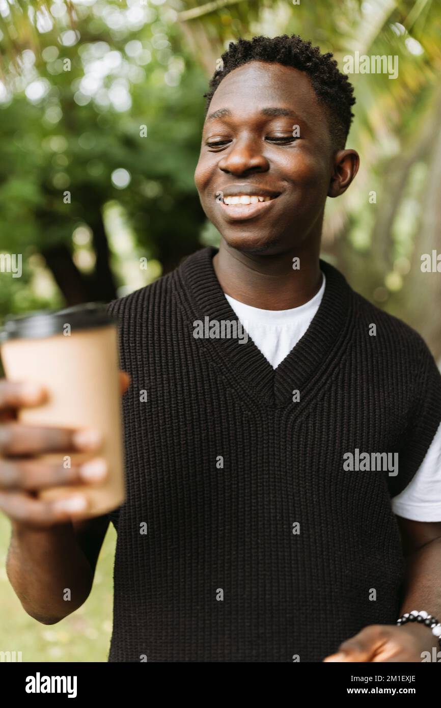Giovane uomo africano sorridente con per andare caffè in strada all'aperto. Giovane studente nero in pausa caffè nel parco Foto Stock
