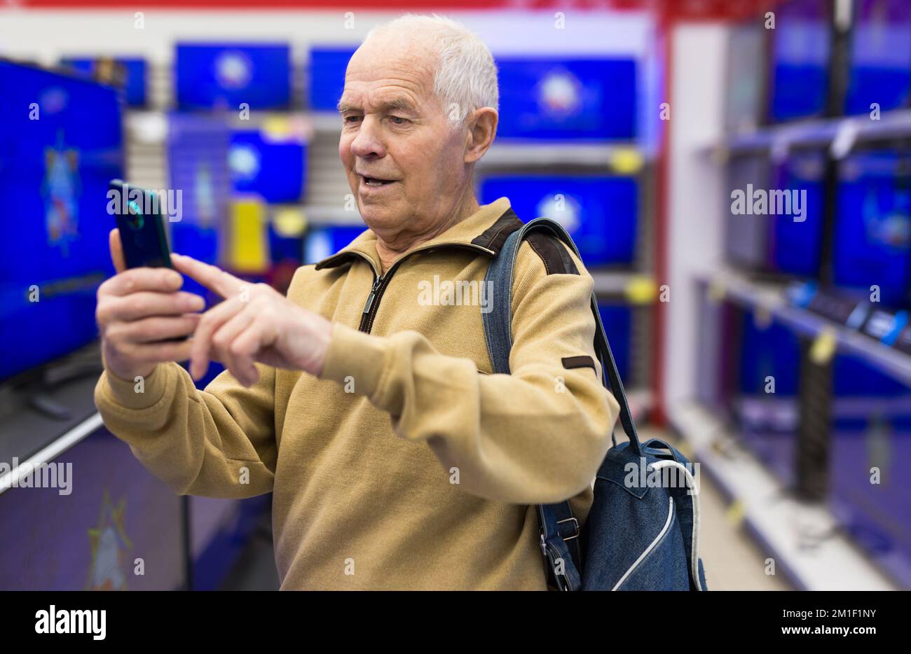 Senor man pensionato a scansione QR code moderno telelavoro digitale con Smart tv in showroom di digital electronic Goods store Foto Stock