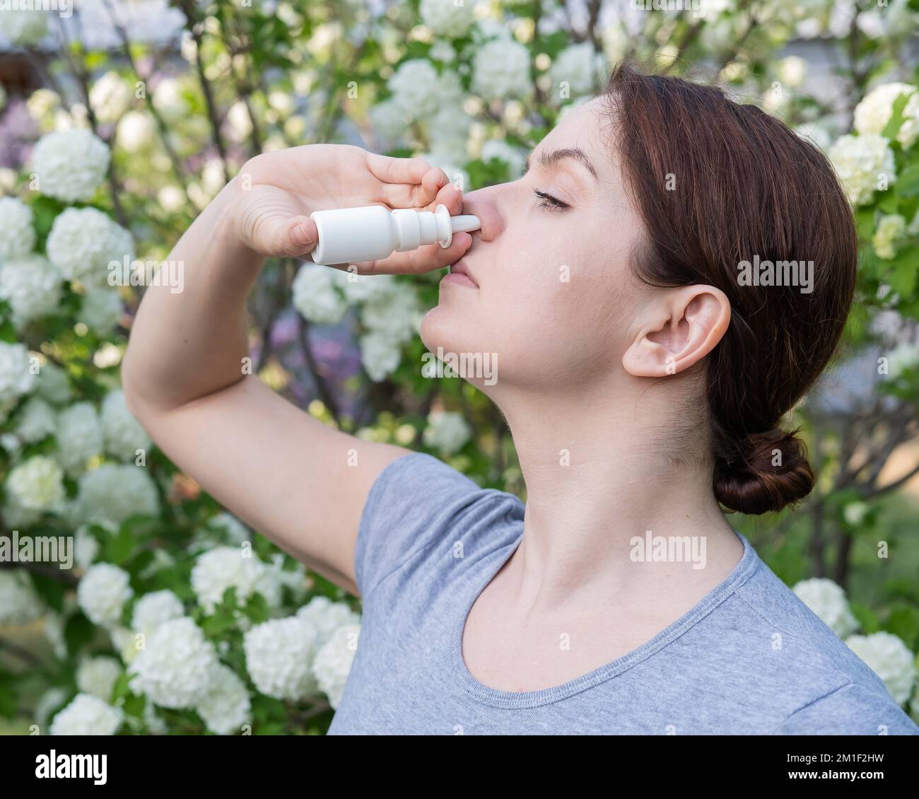 La donna caucasica usa uno spray nasale mentre cammina nel parco. Foto Stock