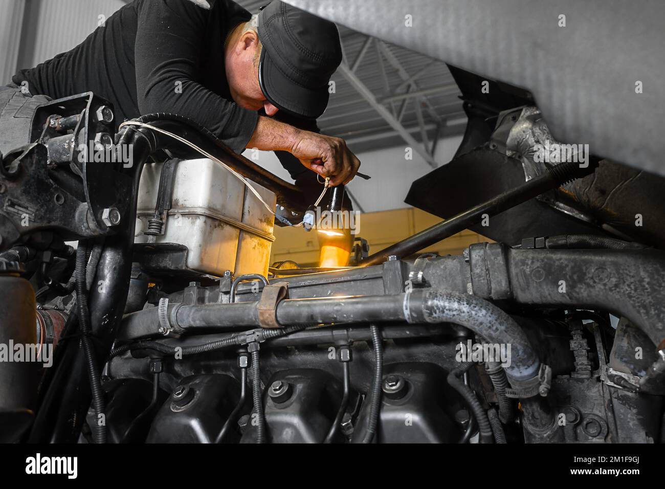 Il meccanico di automobile ripara il camion grande o il trattore in officina. Meccanico professionale ripara il motore del veicolo. Lavoratore genuino.. Foto Stock
