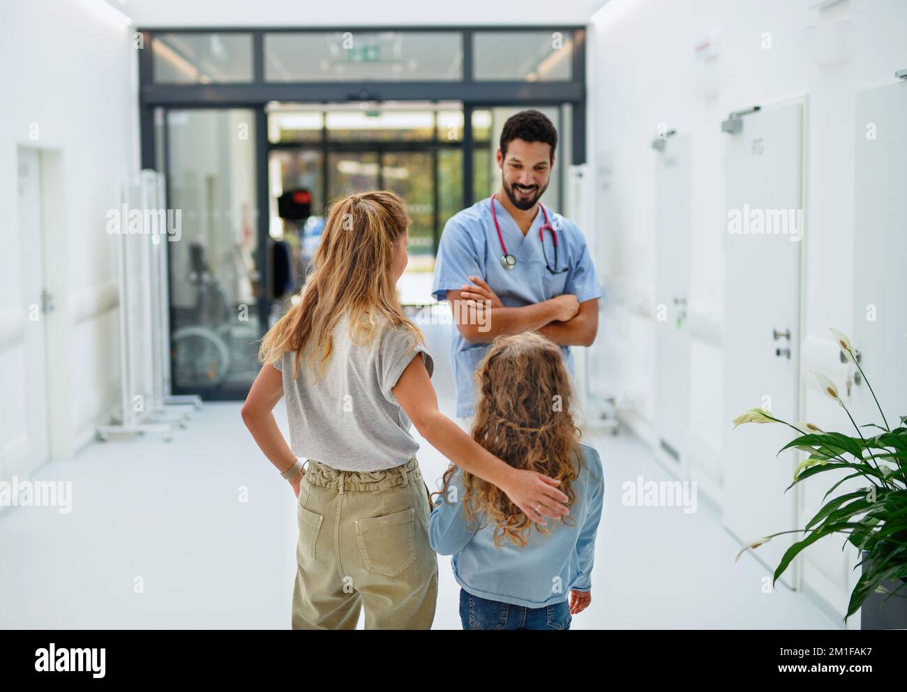 Giovane medico multirazziale che parla con madre di bambina in corridoio ospedale. Foto Stock