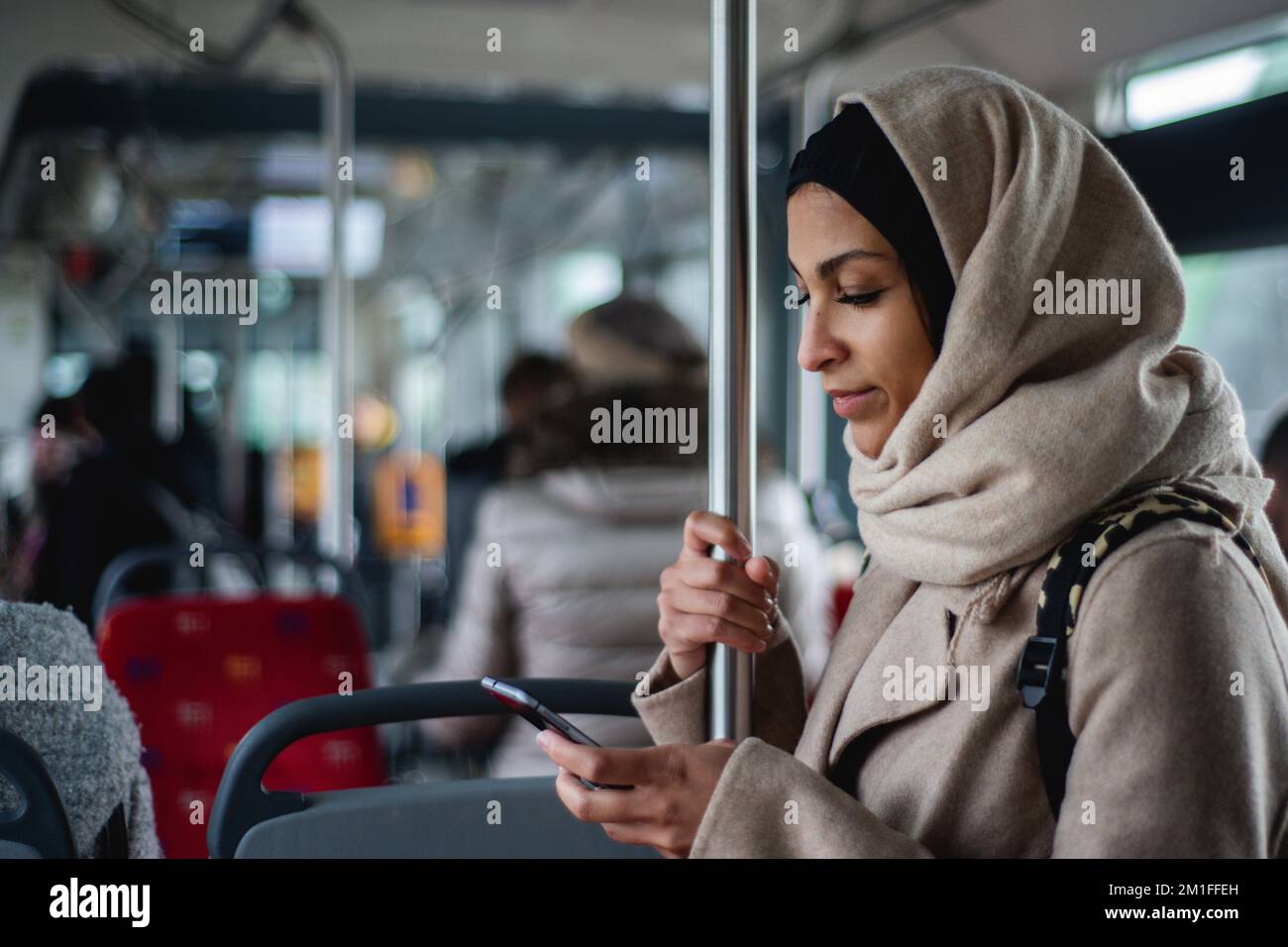 Giovane donna musulmana con smartphone in autobus pubblico. Foto Stock