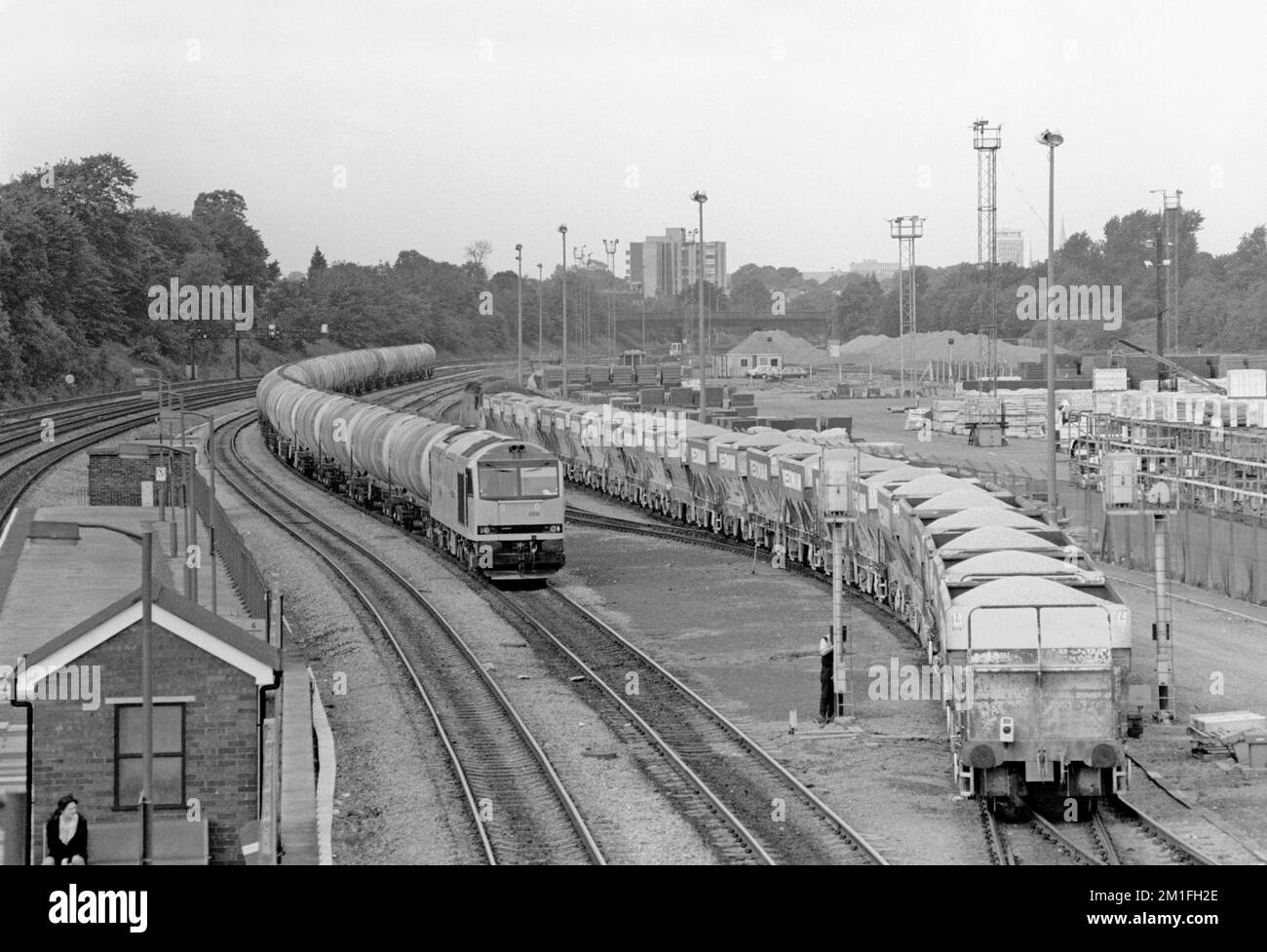 Una locomotiva diesel di classe 60 numero 60056 con un treno di serbatoi di olio del carrello attende tempo ad Acton Yard mentre un treno di tramogge in pietra PGA caricate entra nel cantiere. Linea principale Acton. 10th giugno 1991. Foto Stock