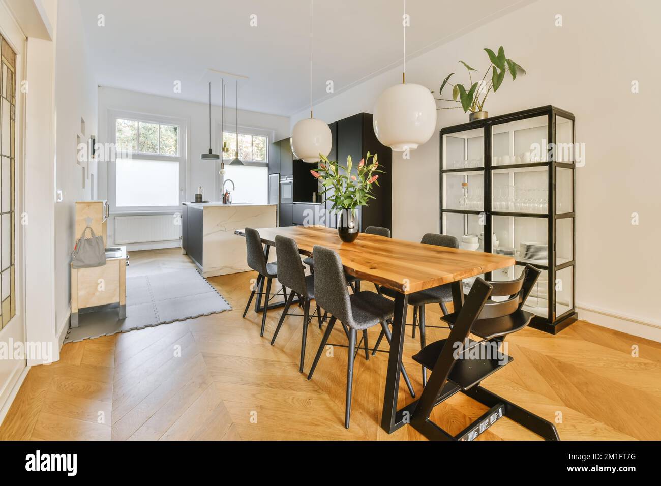 una sala da pranzo con pavimento in legno e pareti bianche vi è un tavolo in legno, sedie nere e una pianta sulla parete Foto Stock