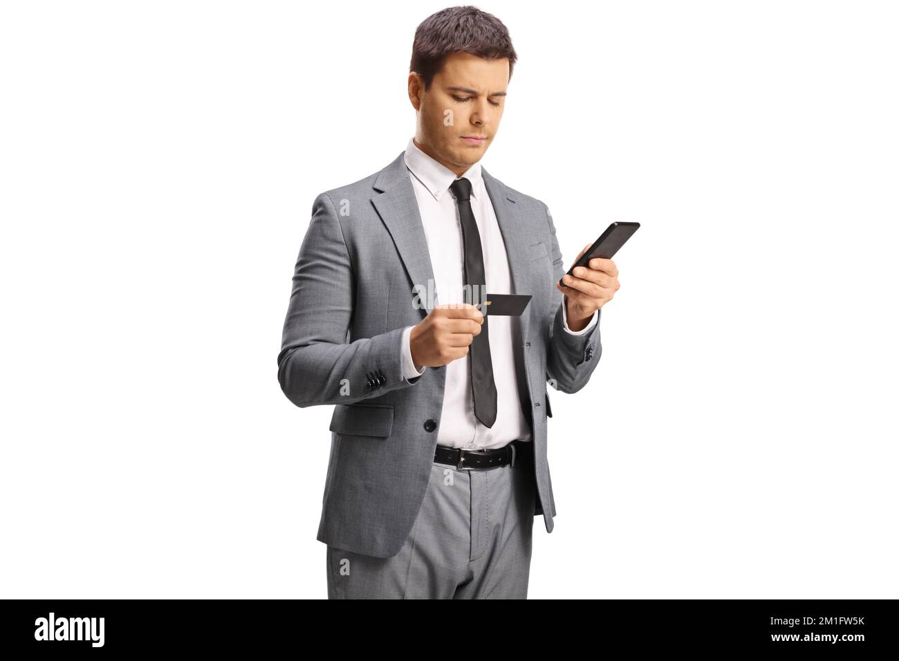 Giovane professionista che tiene uno smartphone e guarda una carta di credito isolata su sfondo bianco Foto Stock