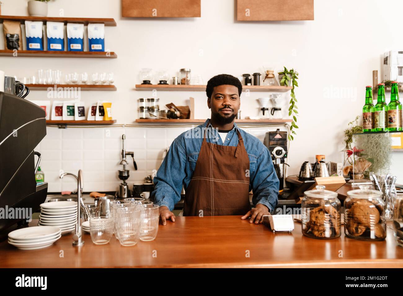 Uomo nero con grembiule sorridente mentre lavora in un bar all'interno Foto  stock - Alamy