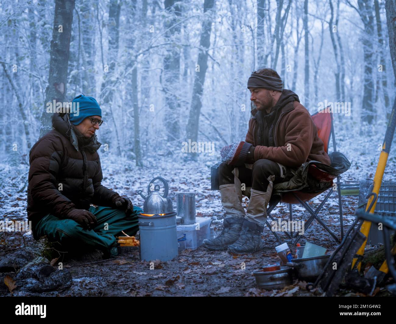 Due campeggiatori invernali che si tengono al caldo con un tè caldo su un fornello a razzo. Foto Stock