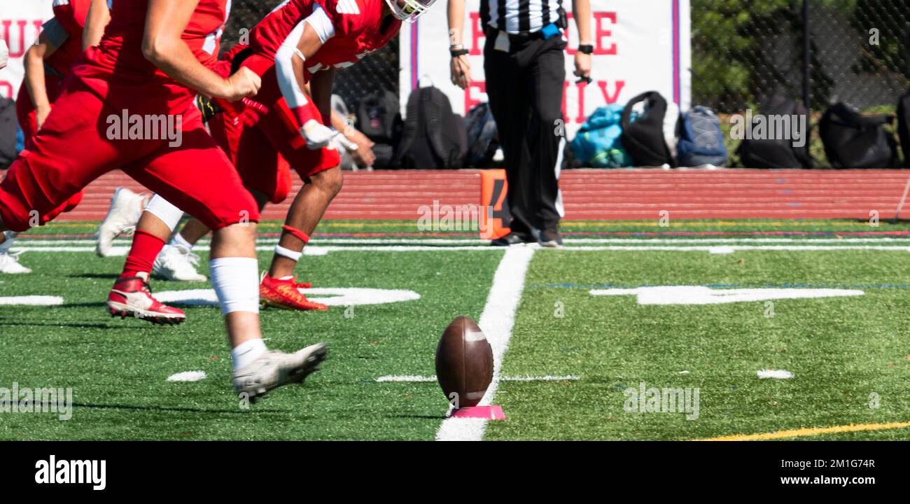 Una squadra di calcio in divise rosse che corre verso la palla su un tee per il calcio d'inizio su un campo verde di erba sintetica. Foto Stock