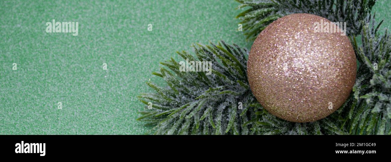 Banner con rametto in abete artificiale con pallina di Natale dorata e brillante su sfondo verde glitter. Spazio di copia. Foto Stock