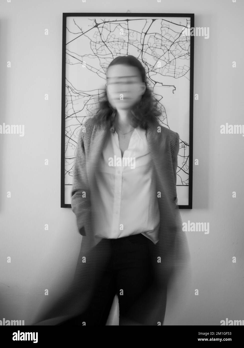 Scala di grigi verticale di una donna che posa sullo sfondo di un'opera d'arte incorniciata sulla parete Foto Stock