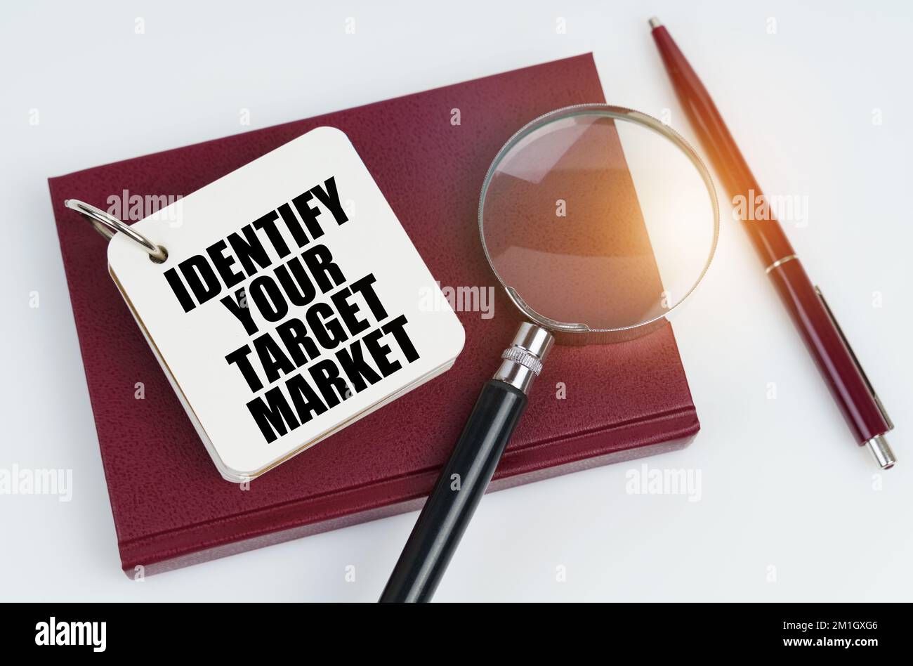 Concetto di business e finanza. Su una superficie bianca si trova un notebook rosso e una penna, nel notebook bianco l'iscrizione - IDENTIFICARE IL VOSTRO MERCATO DI DESTINAZIONE Foto Stock