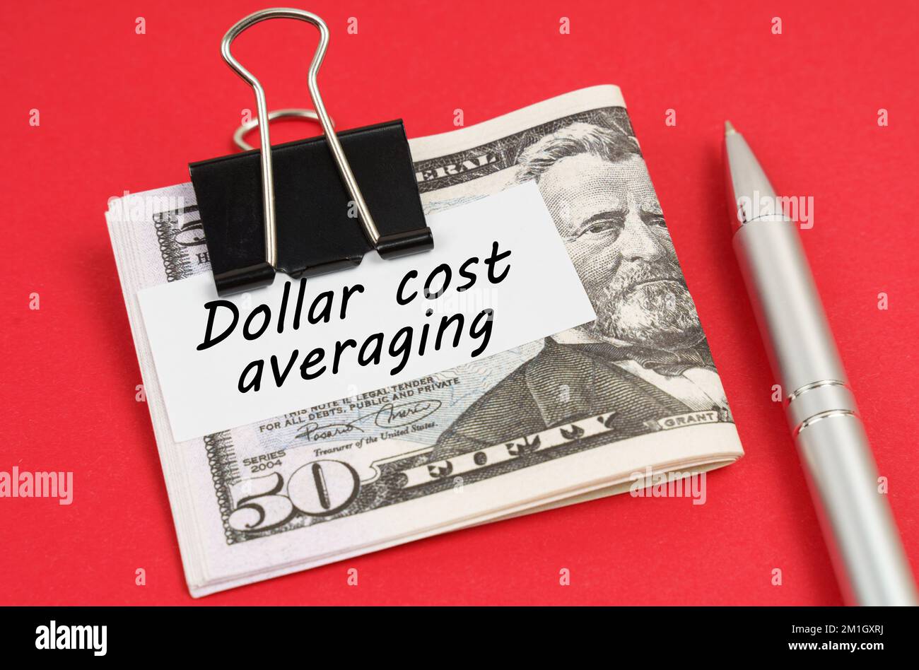 Concetto finanziario e commerciale. Su uno sfondo rosso si trova una penna e dollari bloccati con una clip con l'iscrizione su carta - costo in dollari media Foto Stock