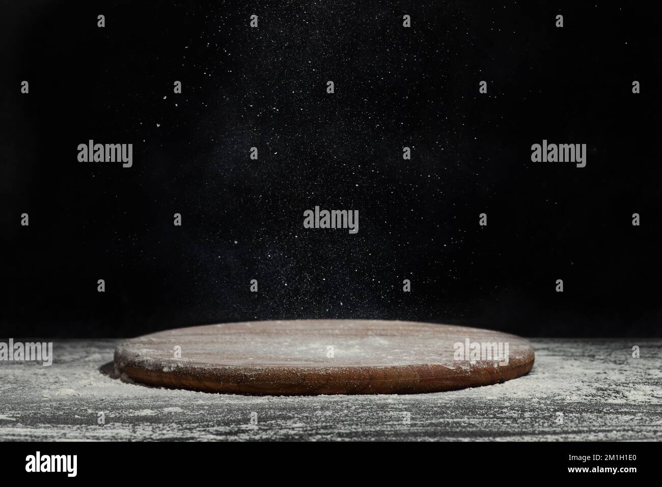 Tavola rotonda in legno per la preparazione degli alimenti con farina su fondo nero Foto Stock