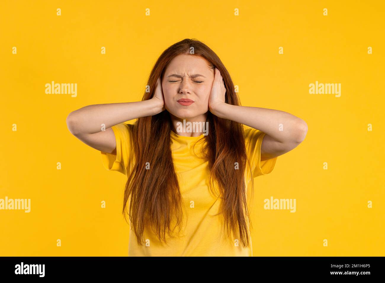 Donna zenzero irritata con orecchie coperte ignorando su sfondo giallo. Adolescente che vieta fastidiosi suoni, grida o rumore. Foto Stock