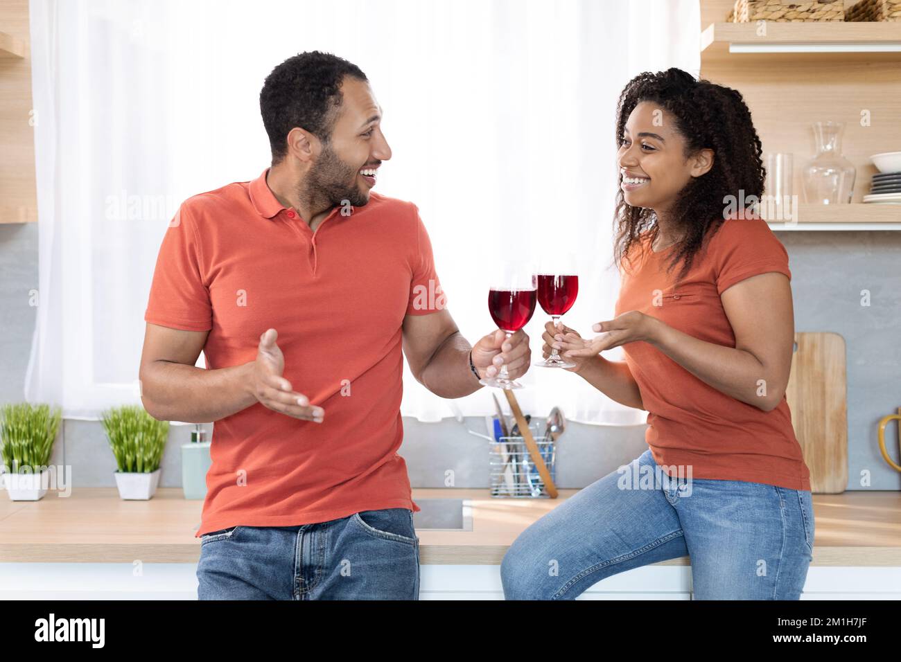 Allegra coppia nera millenaria in t-shirt rossa con bicchieri di vino godere della comunicazione nel tempo libero Foto Stock