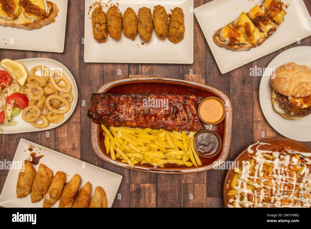 Piatti spagnoli e tapas, toast al formaggio di cipolla e capra, calamari fritti, costolette arrosto, crocchette di prosciutto fatte in casa e empanadas di bonito, hamburger e patatine fritte Foto Stock
