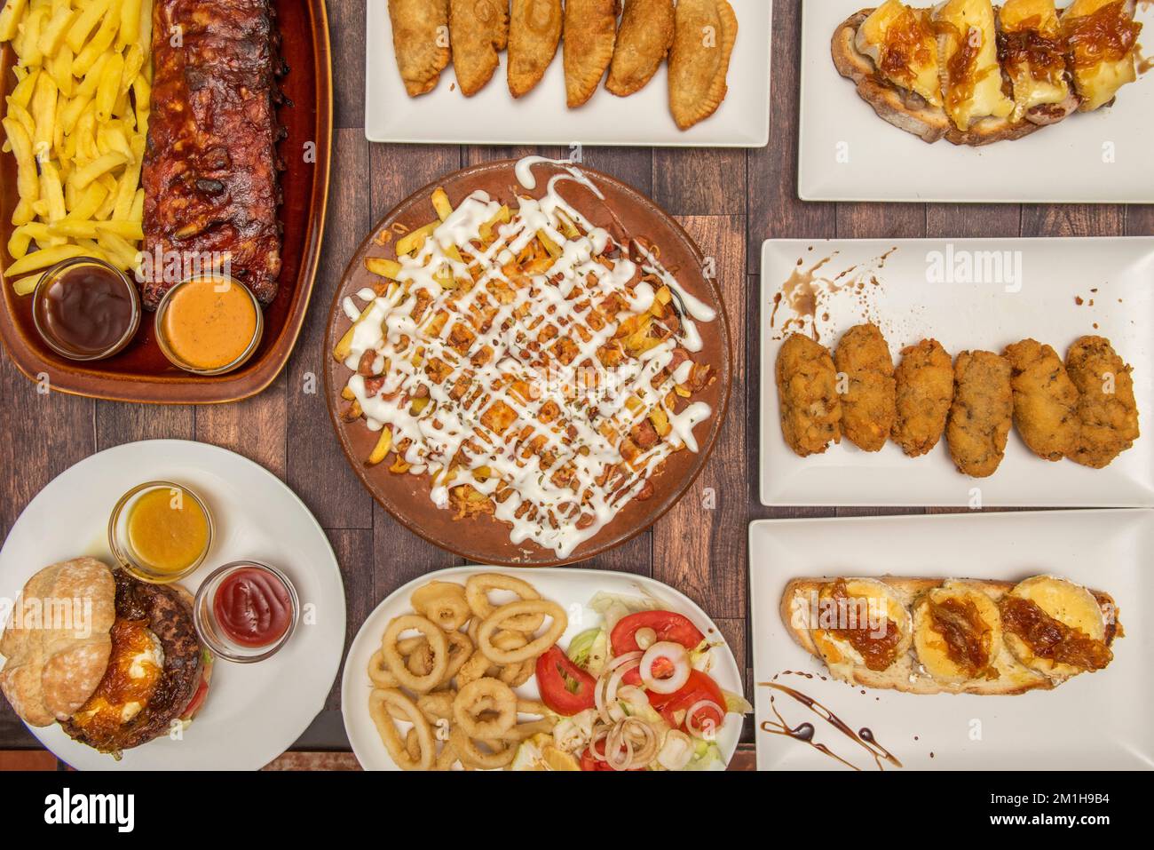 Piatti spagnoli e tapas, toast al formaggio di cipolla e capra, calamari fritti, costolette arrosto, crocchette di prosciutto fatte in casa e empanadas di bonito, hamburger e patatine fritte Foto Stock