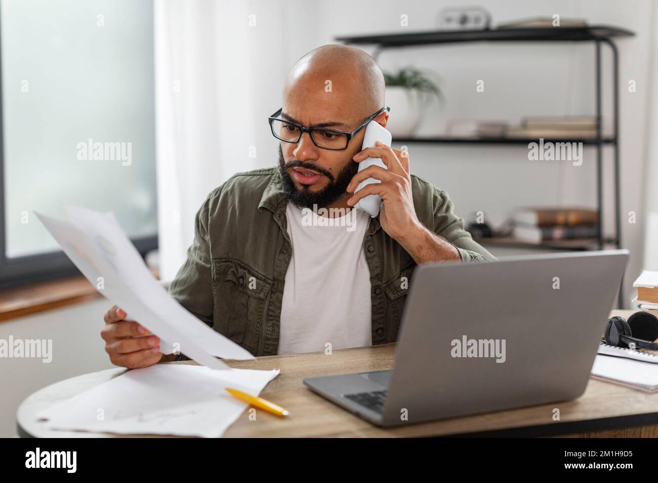 Concetto di comunicazione aziendale. Occupato imprenditore latino maschio che lavora a distanza, parlando al telefono e leggendo un documento Foto Stock