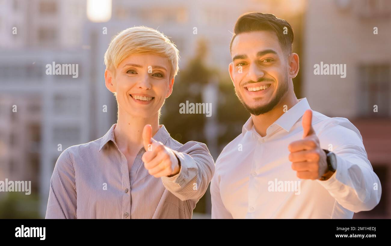 Multietnico due partner di affari colleghi caucasica donna e ispanico uomo ha messo i pollici in piedi all'aperto al tramonto. Coppia multirazziale Foto Stock