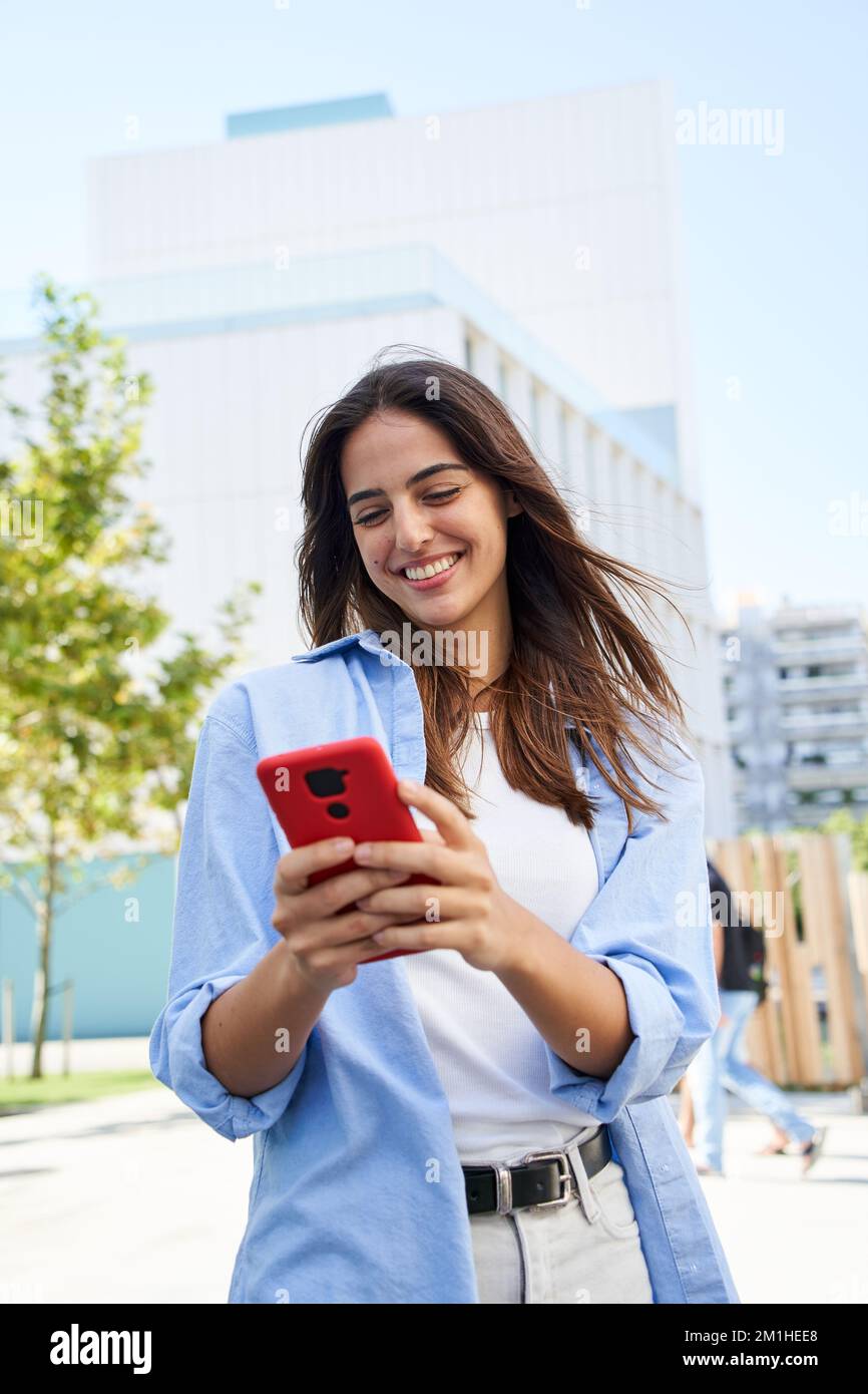 Foto verticale Una giovane ragazza che usa un telefono cellulare all'aperto. Una donna sorridente che flirta attraverso un'app Foto Stock