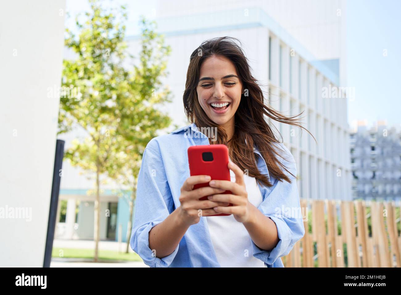 Una giovane ragazza che usa un telefono cellulare all'aperto. Una donna sorridente che flirta attraverso un'app Foto Stock