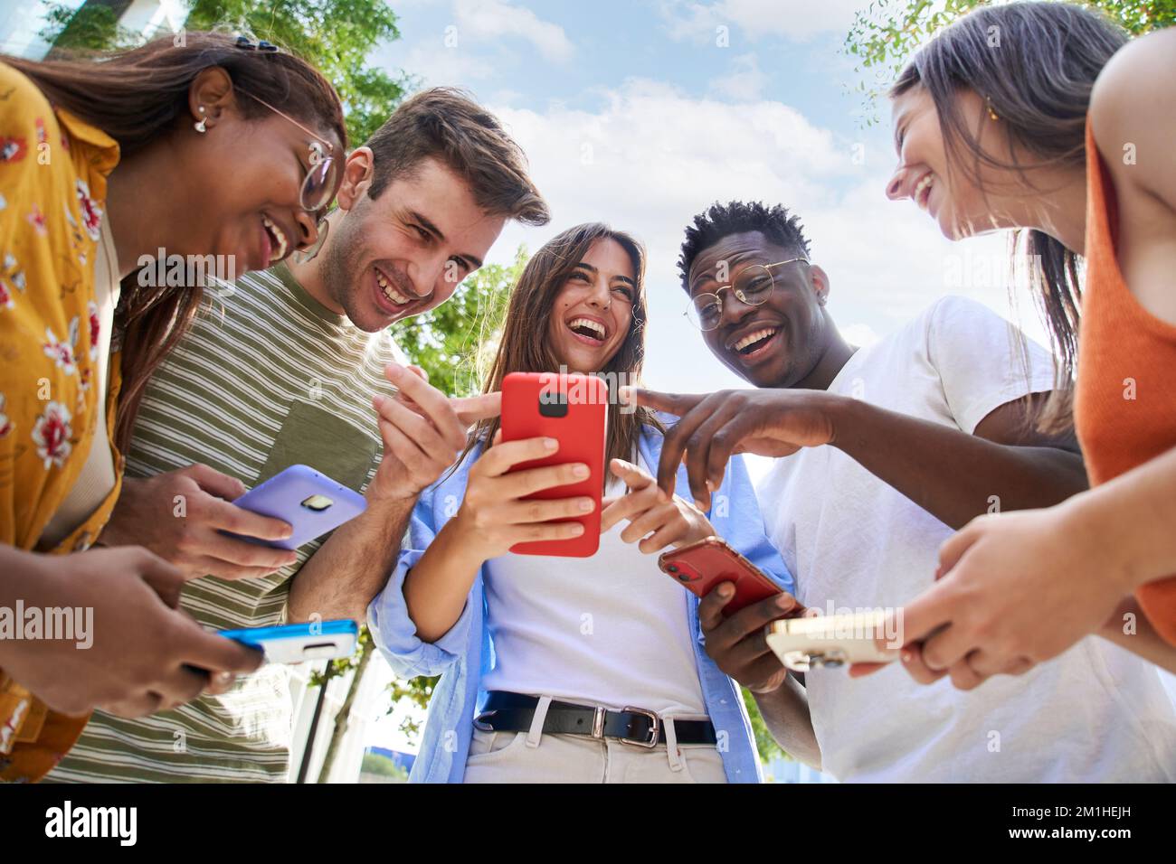 Angolo basso di un gruppo di giovani adolescenti con telefoni cellulari. Volti sorpresi guardando lo schermo Foto Stock