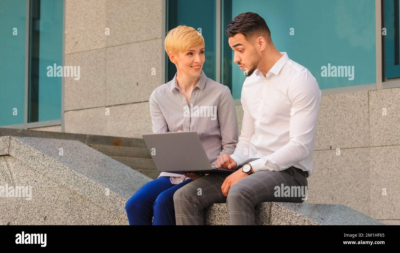 Allegro multietnico coppia colleghi arabo ispanico uomo e donna caucasica in piedi vicino al centro affari in strada all'aperto e. Foto Stock