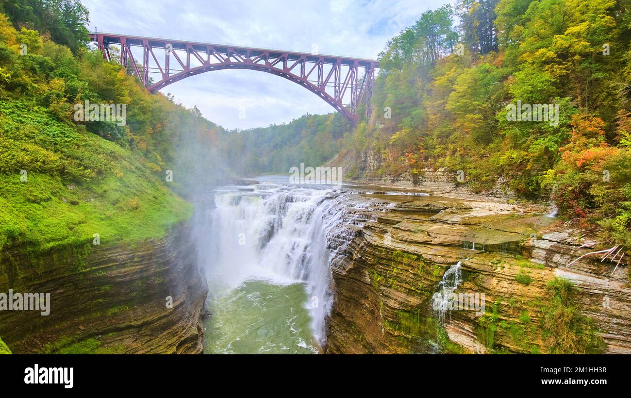 Ponte di acciaio maroon su una splendida cascata che attraversa scogliere a strati in una lussureggiante foresta verde Foto Stock