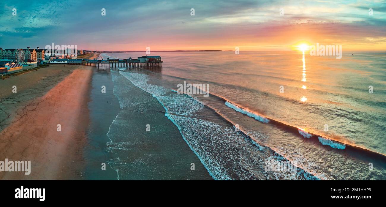 Molo in legno, spiaggia e negozi con onde oceaniche dall'alto durante l'alba Foto Stock
