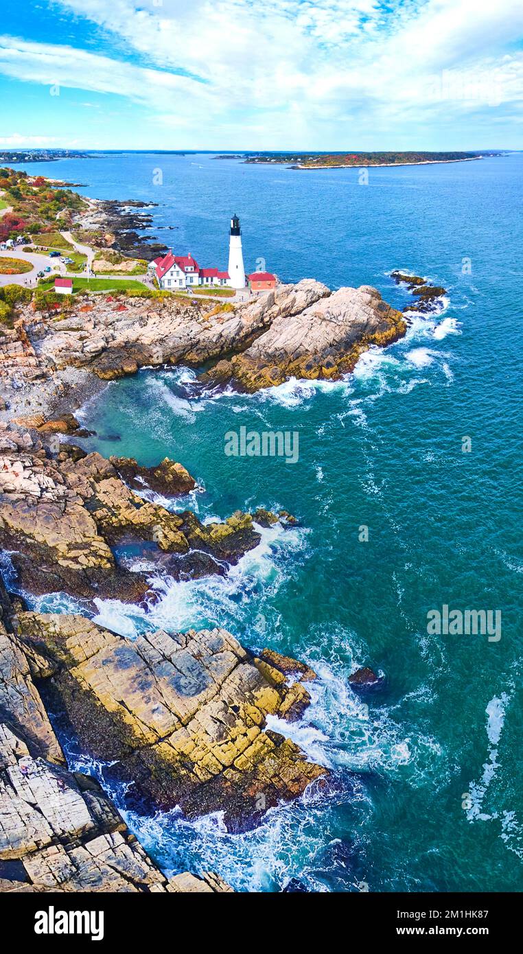 Le onde oceaniche si infrangono sulla costa rocciosa del Maine con un grande faro sul bordo Foto Stock