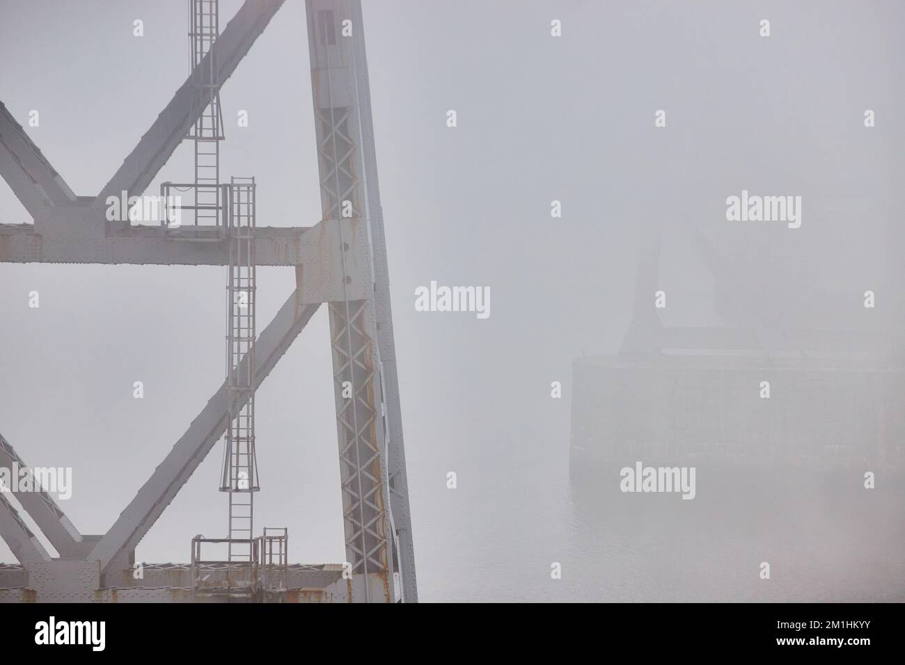 Sostegni pilastri di vecchio ponte di acciaio con scale che sbiadono in condizioni meteorologiche estreme nebbia mattina Foto Stock