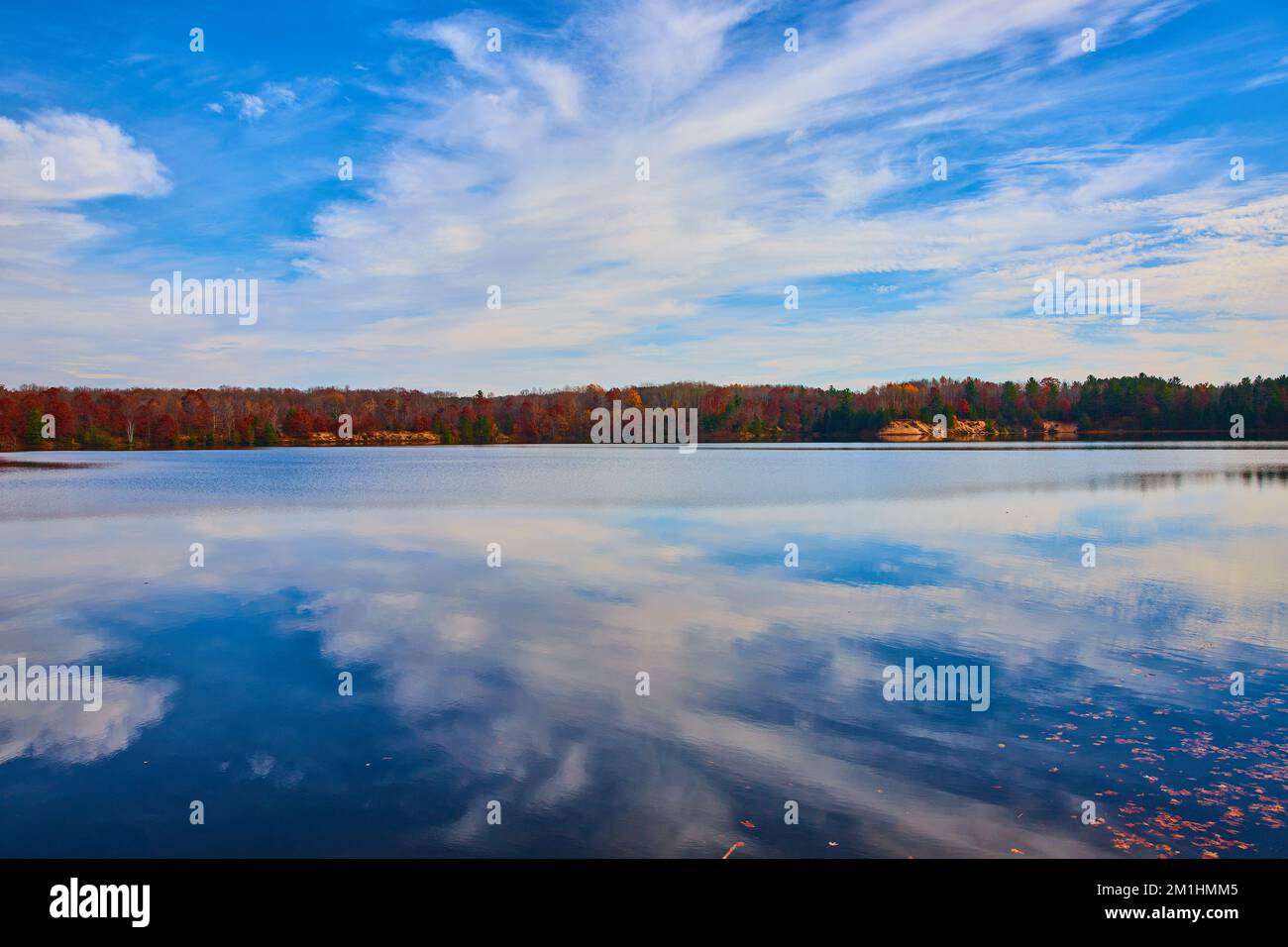 Lago liscio che riflette il cielo blu e gli alberi di caduta che costeggiano la costa Foto Stock