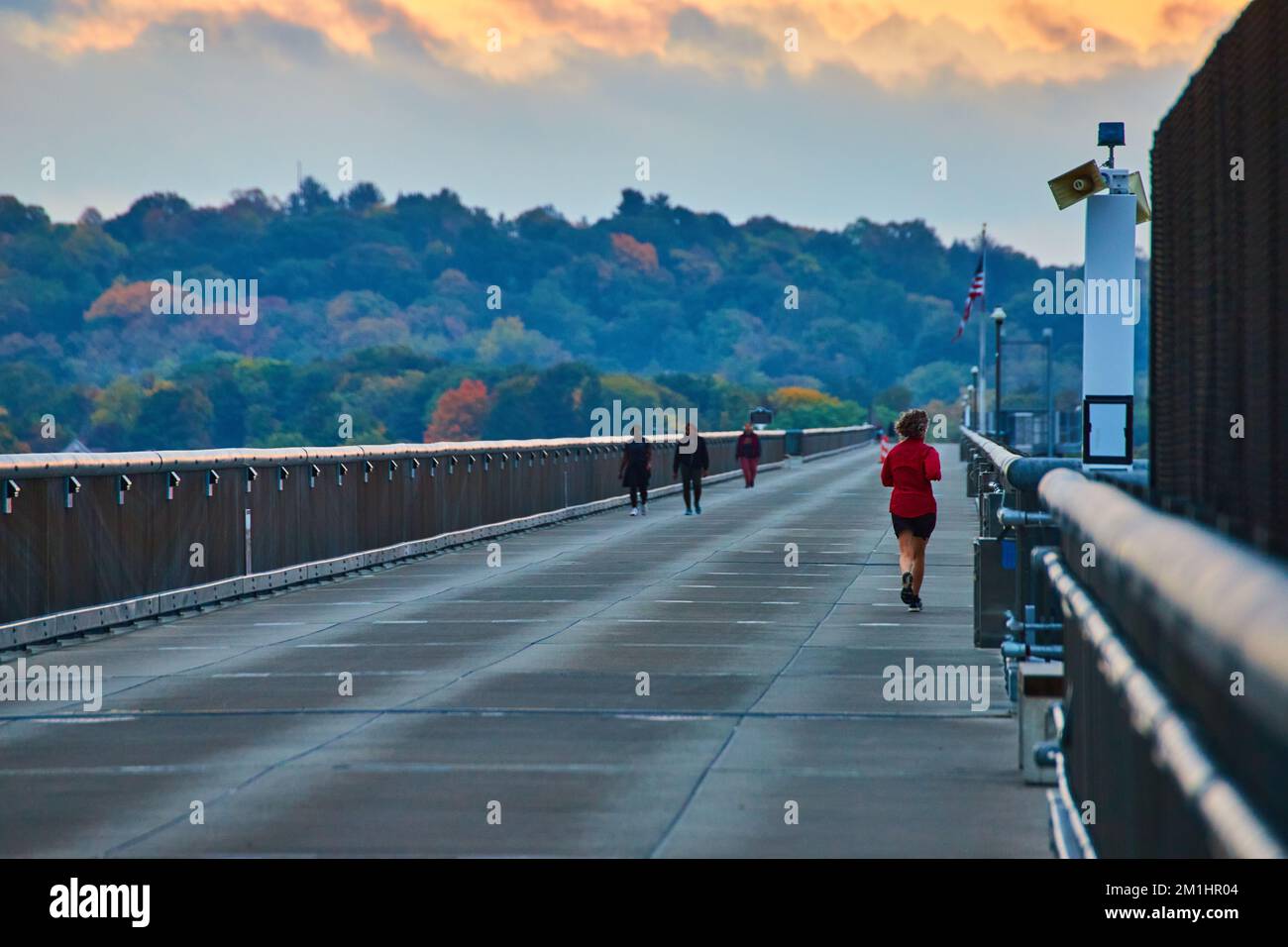 Joggers che corrono lungo il lungo ponte di cemento passerella con foreste sullo sfondo Foto Stock