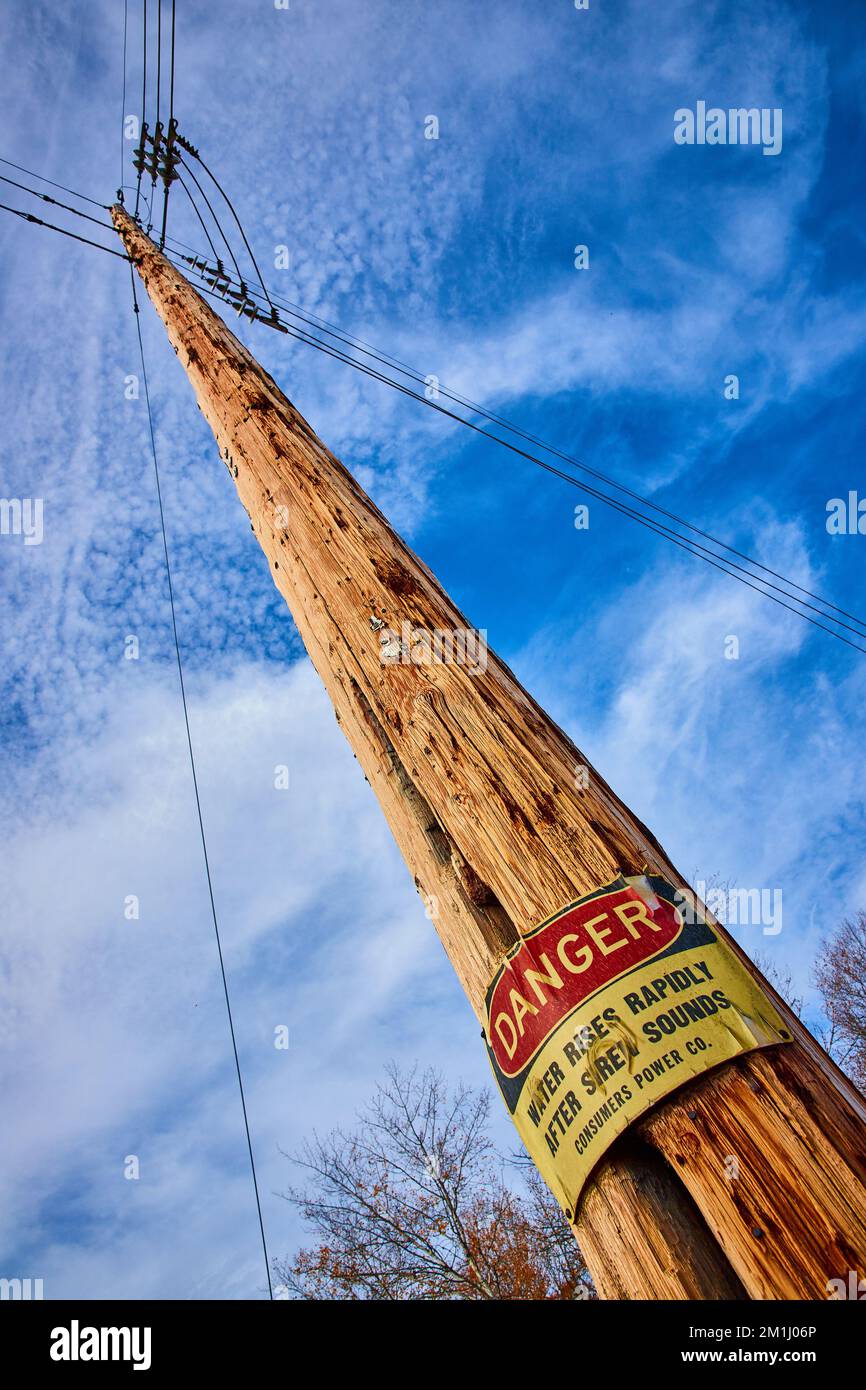 Guardando in su al palo del telefono con grande cartello DI PERICOLO postato circa l'area di inondazione Foto Stock