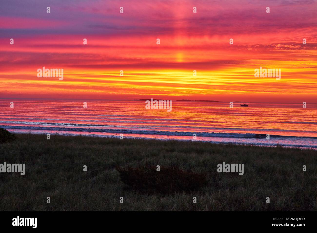 Luce dorata dell'alba sulla spiaggia della costa orientale con onde che si infrangono e navi da pesca in lontananza Foto Stock