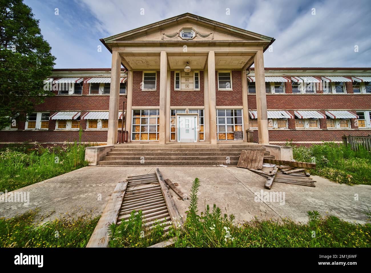 Ingresso a un vecchio edificio abbandonato con pilastri in pietra, superficie in mattoni e campi coltivati in eccesso Foto Stock