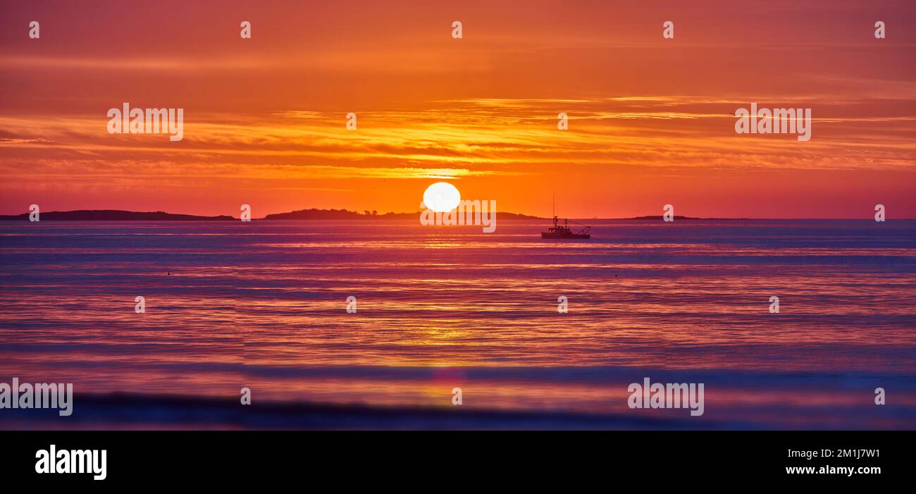 Luce dorata sull'oceano della costa orientale con alba e dettagli del sole e della nave da pesca in lontananza Foto Stock