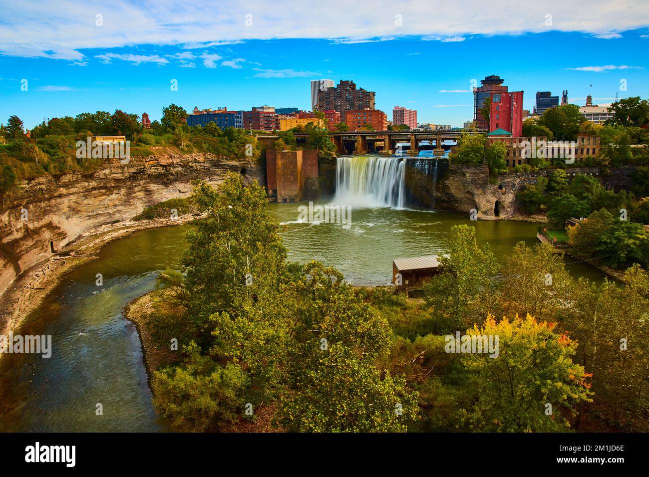 Lo skyline di Rochester lungo il fiume e le scogliere con una cascata che scorre oltre il ponte Foto Stock