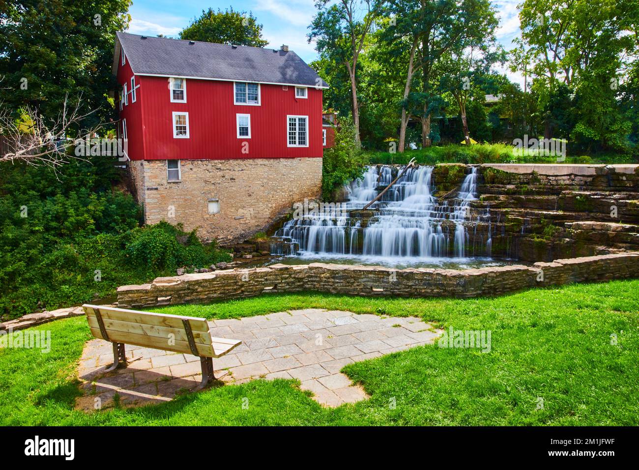 Casa rossa lungo il fiume in città con cascata e piattaforma di osservazione panca del parco Foto Stock