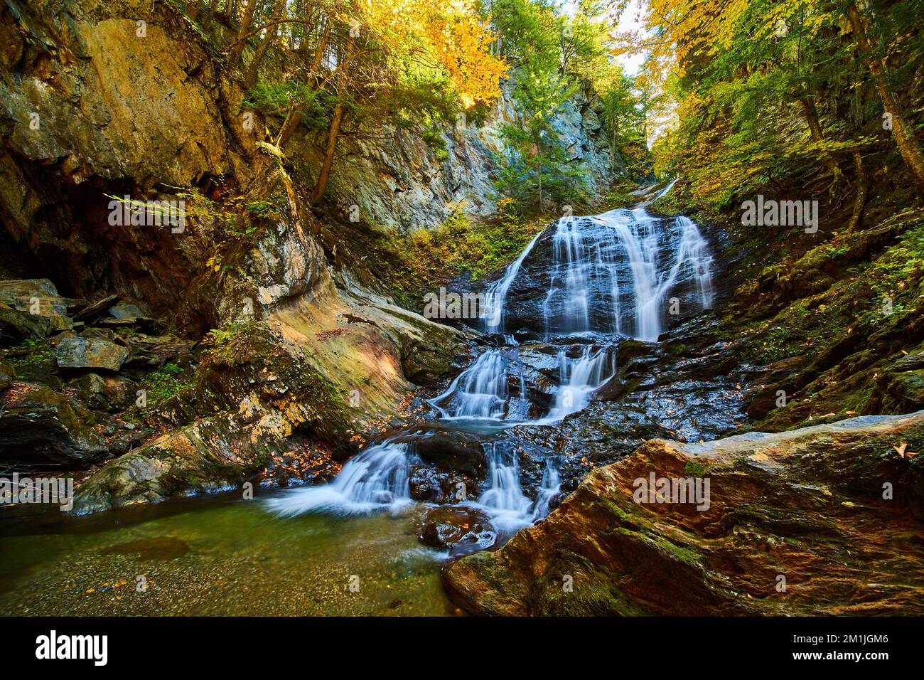 Le foglie di caduta coprono la gola rocciosa con la cascata infuriante e gli alberi nel fogliame di picco Foto Stock