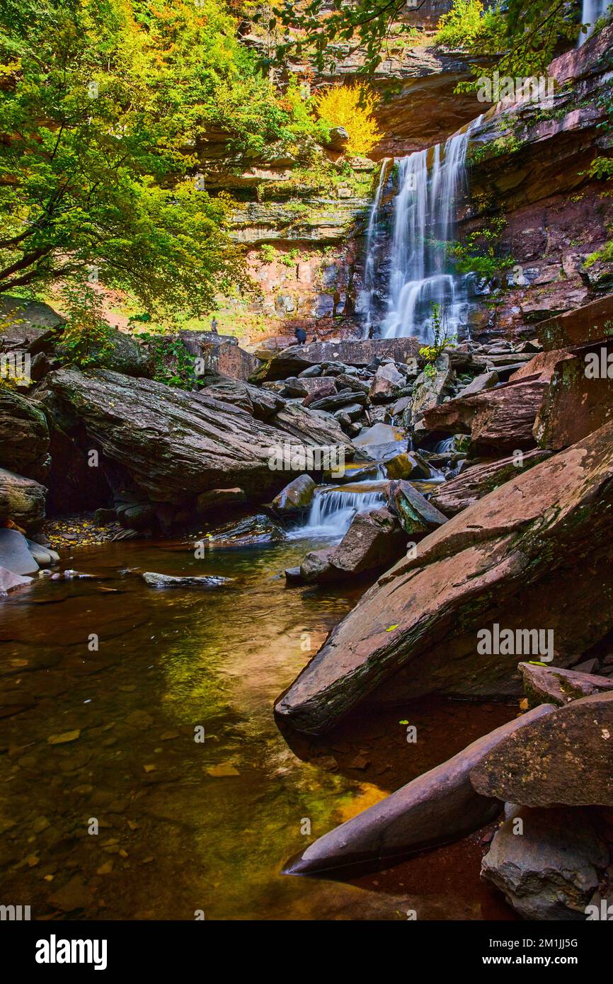Bella luce soffusa di cascate sopra le scogliere con massi e fiume calmo durante il fogliame autunnale Foto Stock