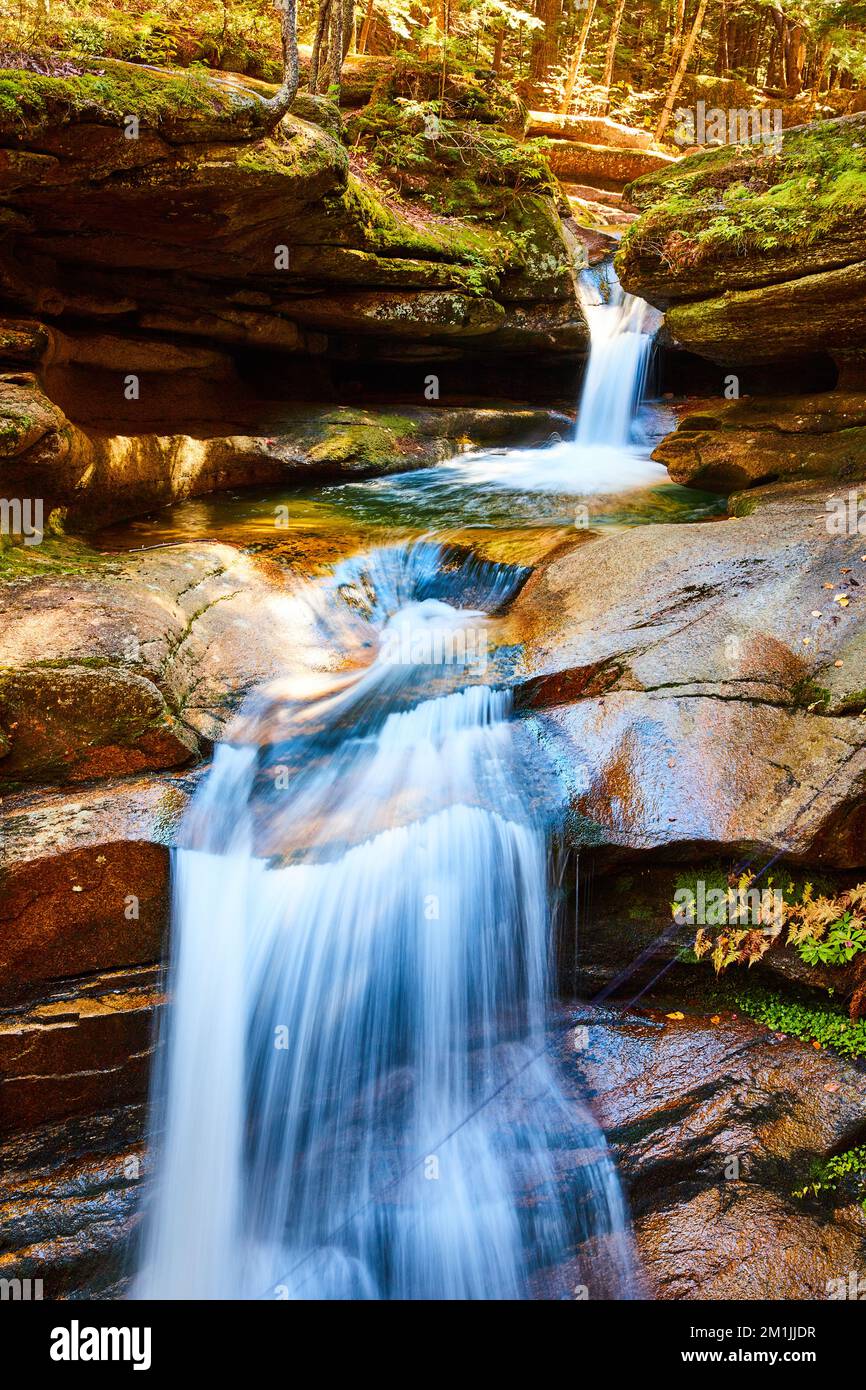 Cascate con movimento sfocato attraverso la tranquilla foresta di caduta con rocce e foresta mossy Foto Stock