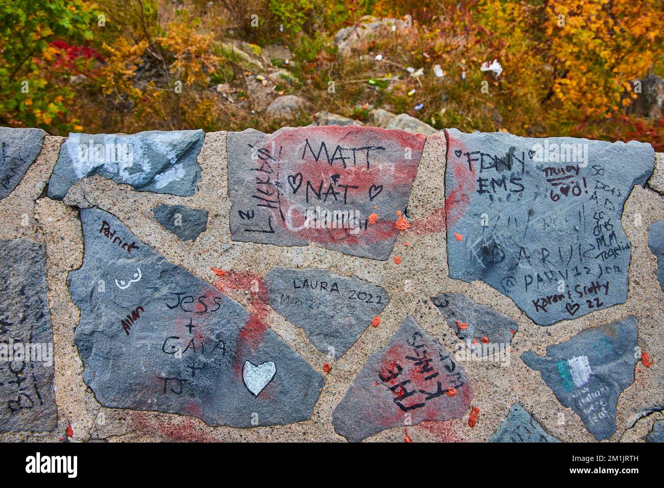 Guardando giù su un muro di pietra coperto di graffiti con caduta alla foresta Foto Stock