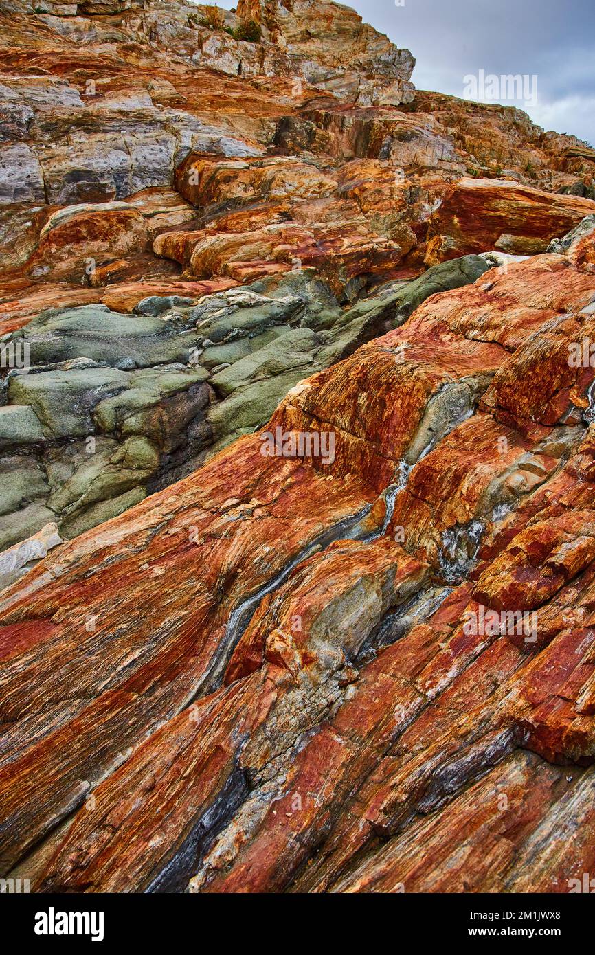 Gli strati di roccia coprono la costa del Maine con strati arancioni e venature di quarto Foto Stock