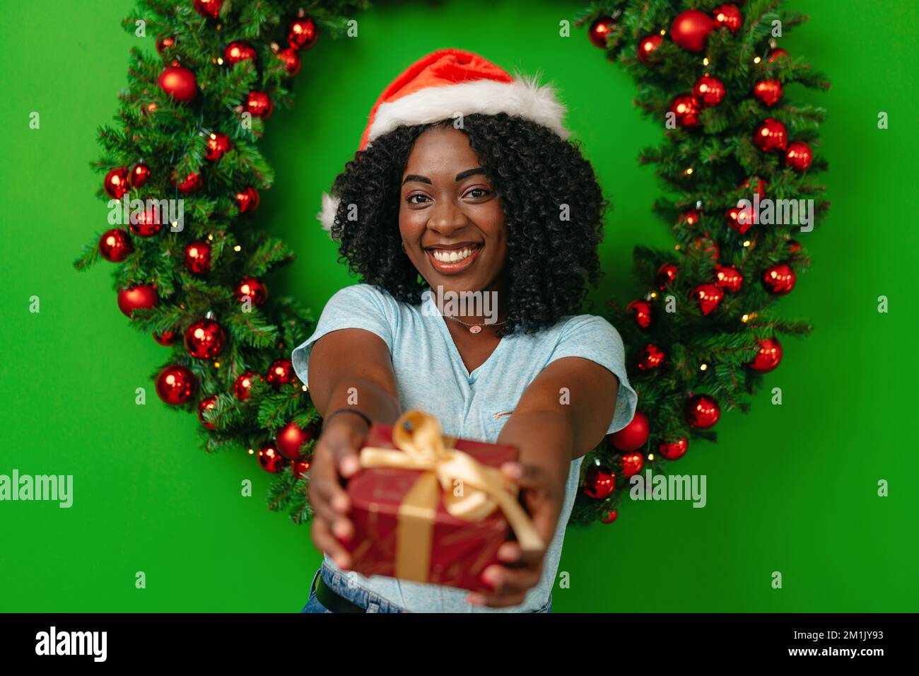 Donna africana sorridente in piedi contro decorazione di corona di Natale a casa Foto Stock