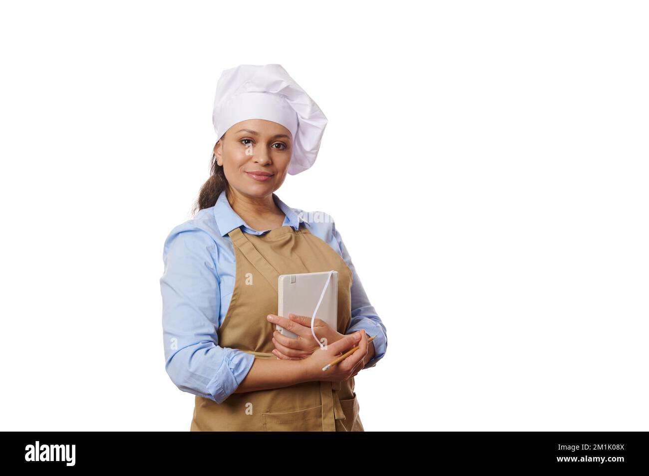 Fiducioso ritratto di affascinante donna ispanica pasticciere chef con un blocco note, isolato su sfondo bianco. Copia spazio pubblicitario Foto Stock